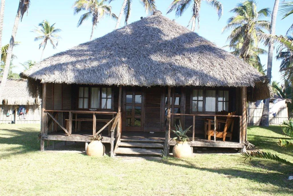 Thatchedroof wooden cabin with porch in a tropical setting with palm trees