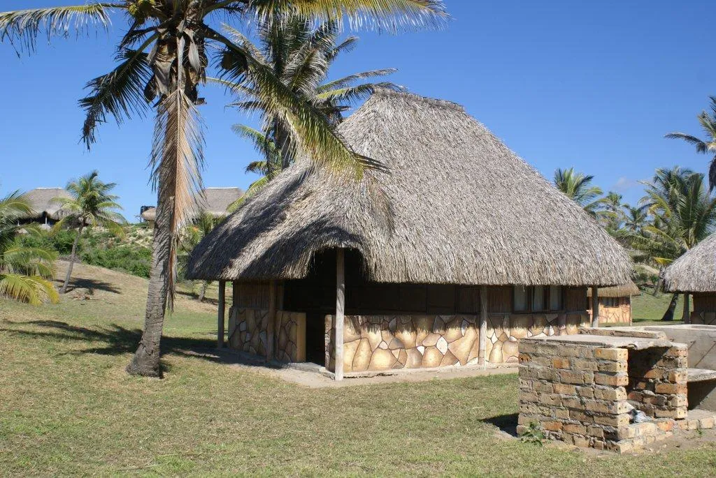 Thatchedroof hut with stone base in a tropical setting with palm trees