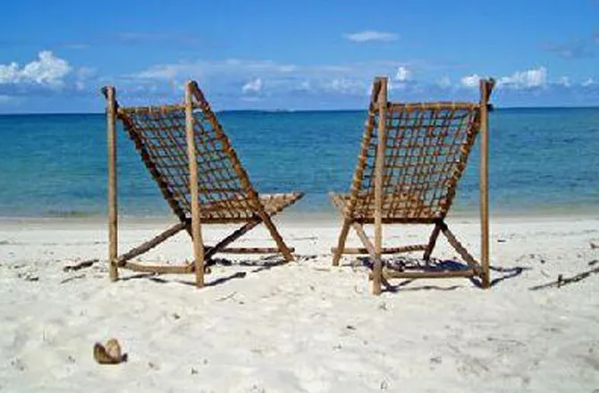 Two wooden lounge chairs on a sandy beach with ocean in the background