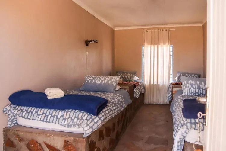 Two single beds in a small simply furnished bedroom with tiled floor