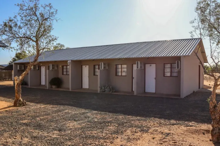 Singlestory building with multiple doors and windows surrounded by sparse trees and gravel