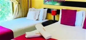 Hotel room with two beds one with red pillows and a bedside table