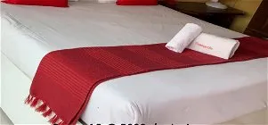 White bed with red runner and towels red pillows wooden nightstand