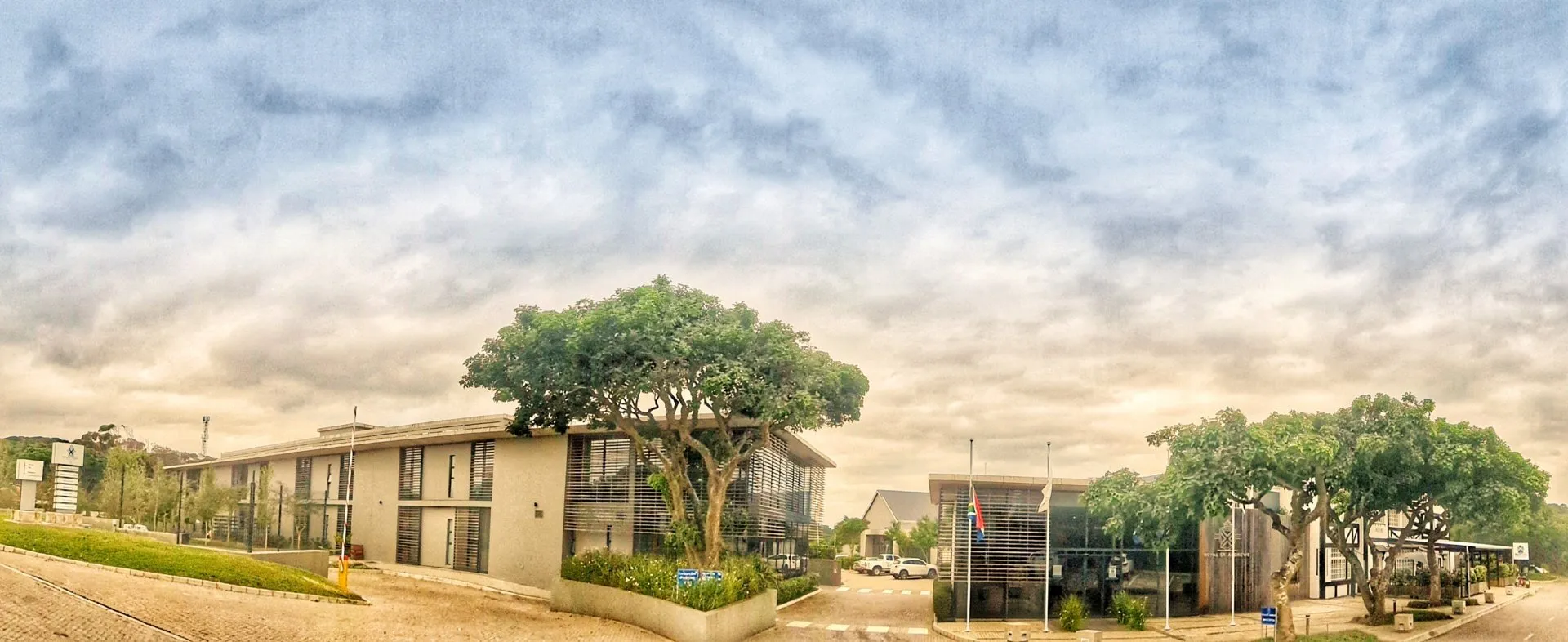 Modern buildings with large windows surrounded by trees under a cloudy sky