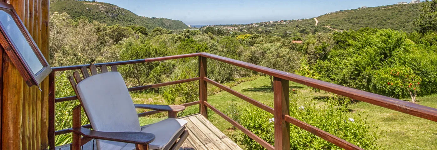 Wooden balcony with a chair overlooking a lush green valley