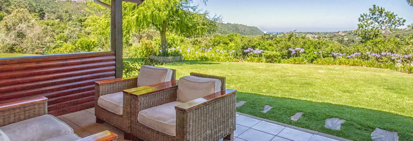 Two wicker chairs on a patio overlooking a lush garden and distant hills