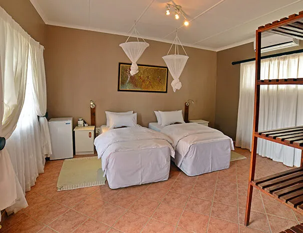 Two single beds with mosquito nets in a tiled bedroom with white curtains