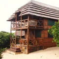Wooden house with a thatched roof surrounded by greenery and sand