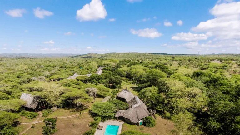 Aerial view of thatchedroof lodges in a lush green landscape