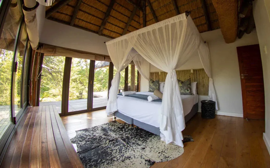 Bedroom with large bed canopy wooden floor and large windows showing greenery