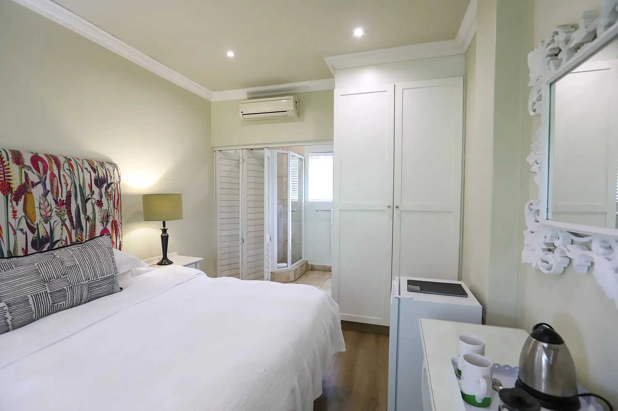 Bright bedroom with white bed patterned headboard and small kitchenette area