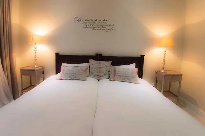 Cozy bedroom with neatly made bed two bedside lamps and wall quote