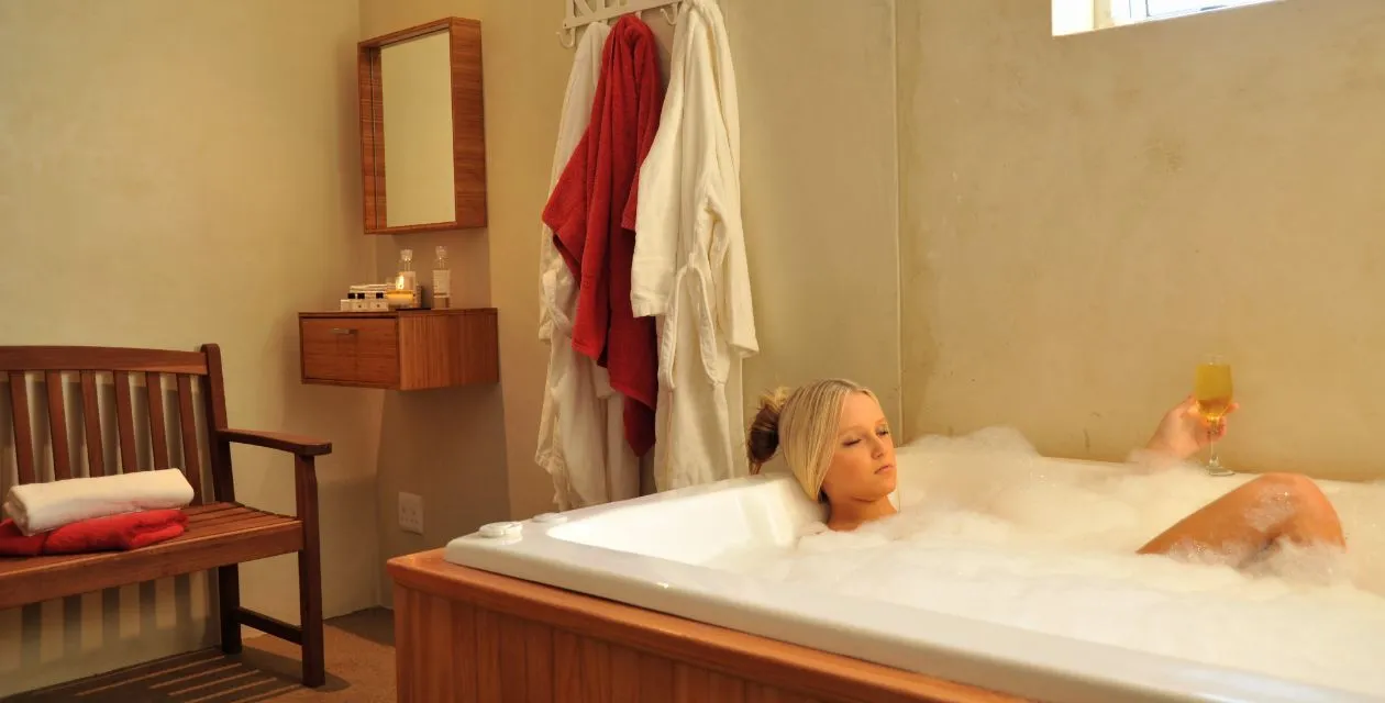 Woman relaxing in a bubble bath with a drink in a cozy bathroom
