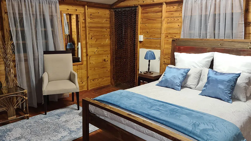 Wooden bedroom with a large bed blue pillows and a beige armchair