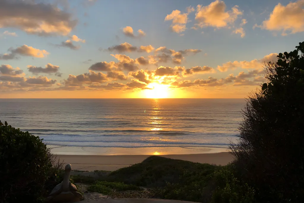 Sunset over the ocean with scattered clouds and beach in the foreground