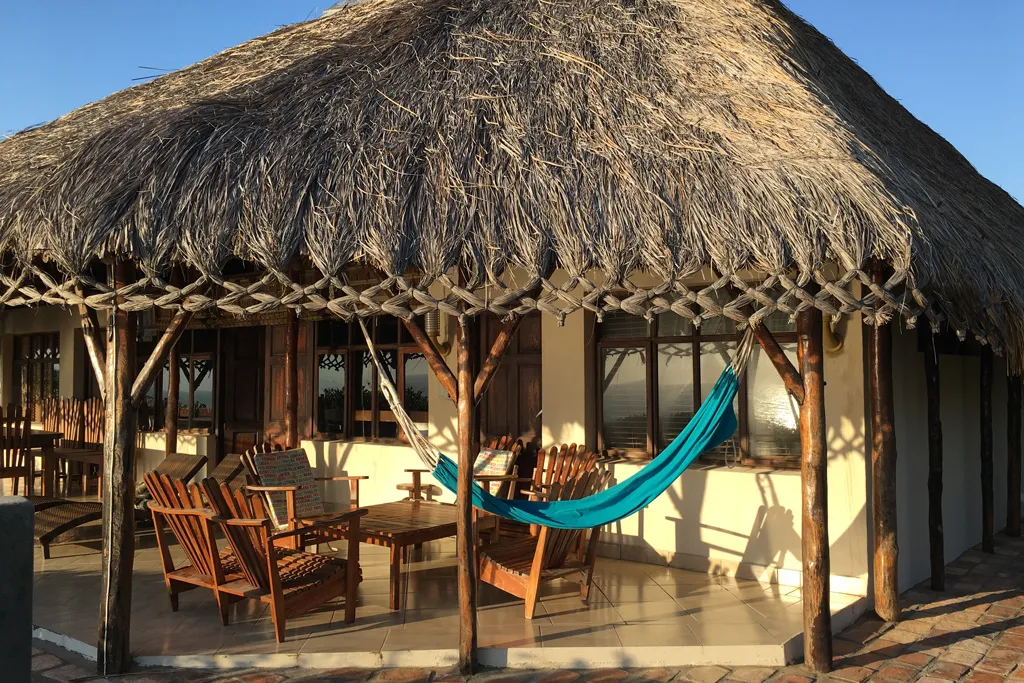 Thatchedroof patio with wooden chairs table and blue hammock