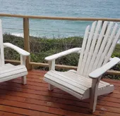 Two white chairs on a wooden deck overlooking the ocean