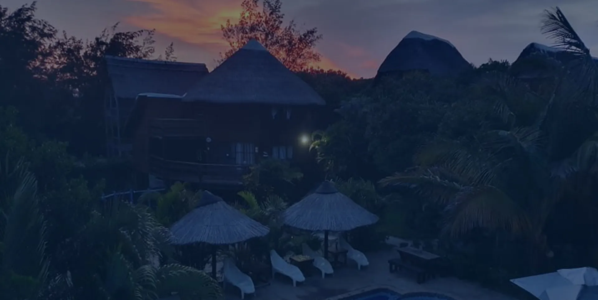 Tropical resort with thatchedroof huts and lounge chairs at sunset