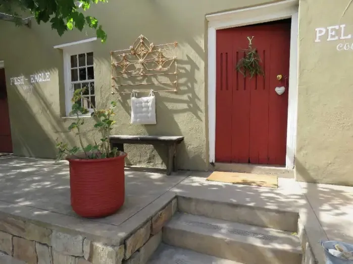 Red door of a cottage with a potted plant and bench outside