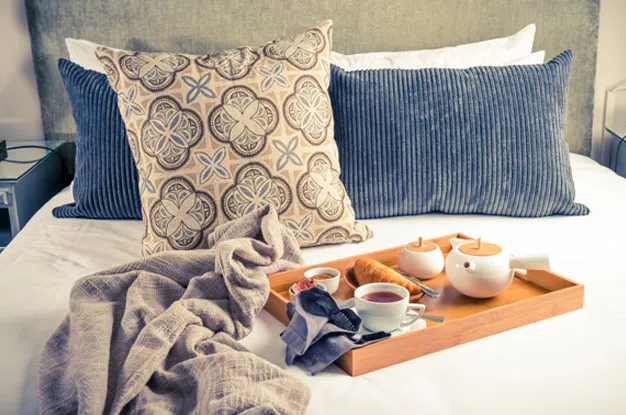 Breakfast tray on bed with pillows blanket and decorative pillow in background