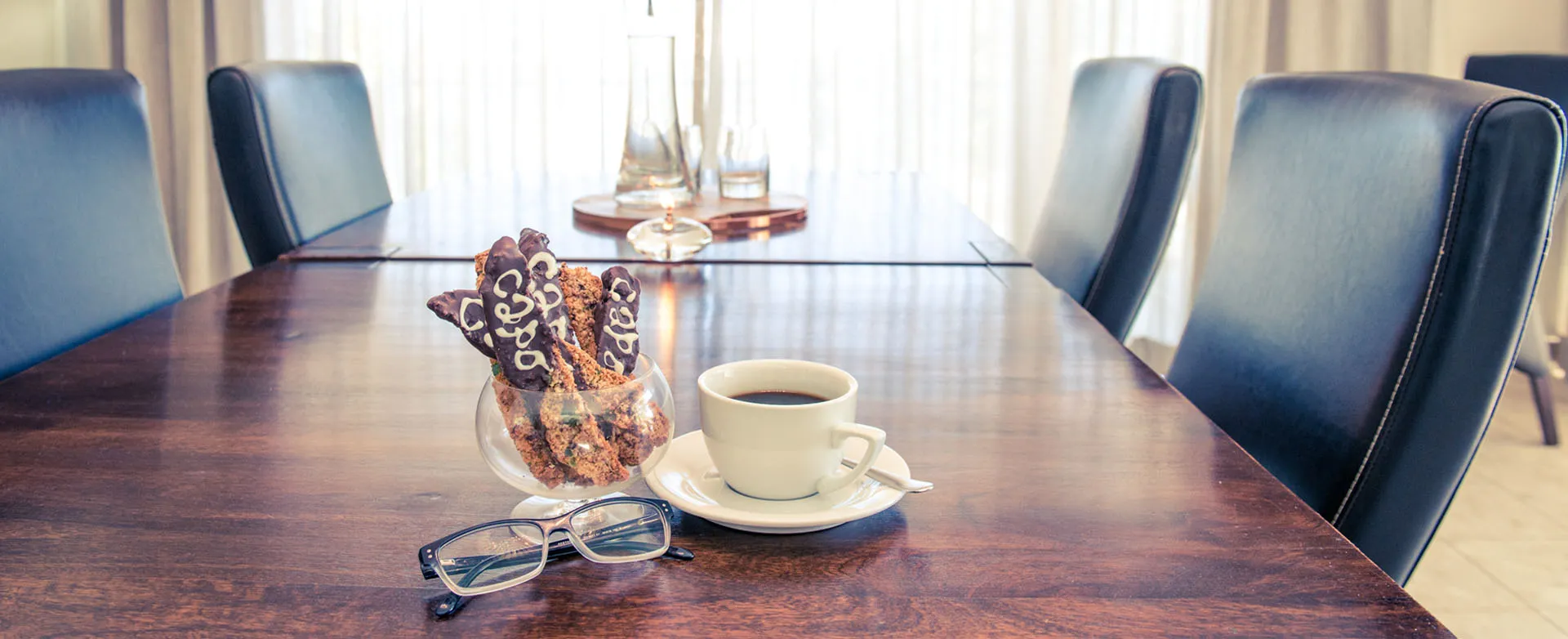 Wooden table with coffee cup cookies glasses and chairs in a bright room