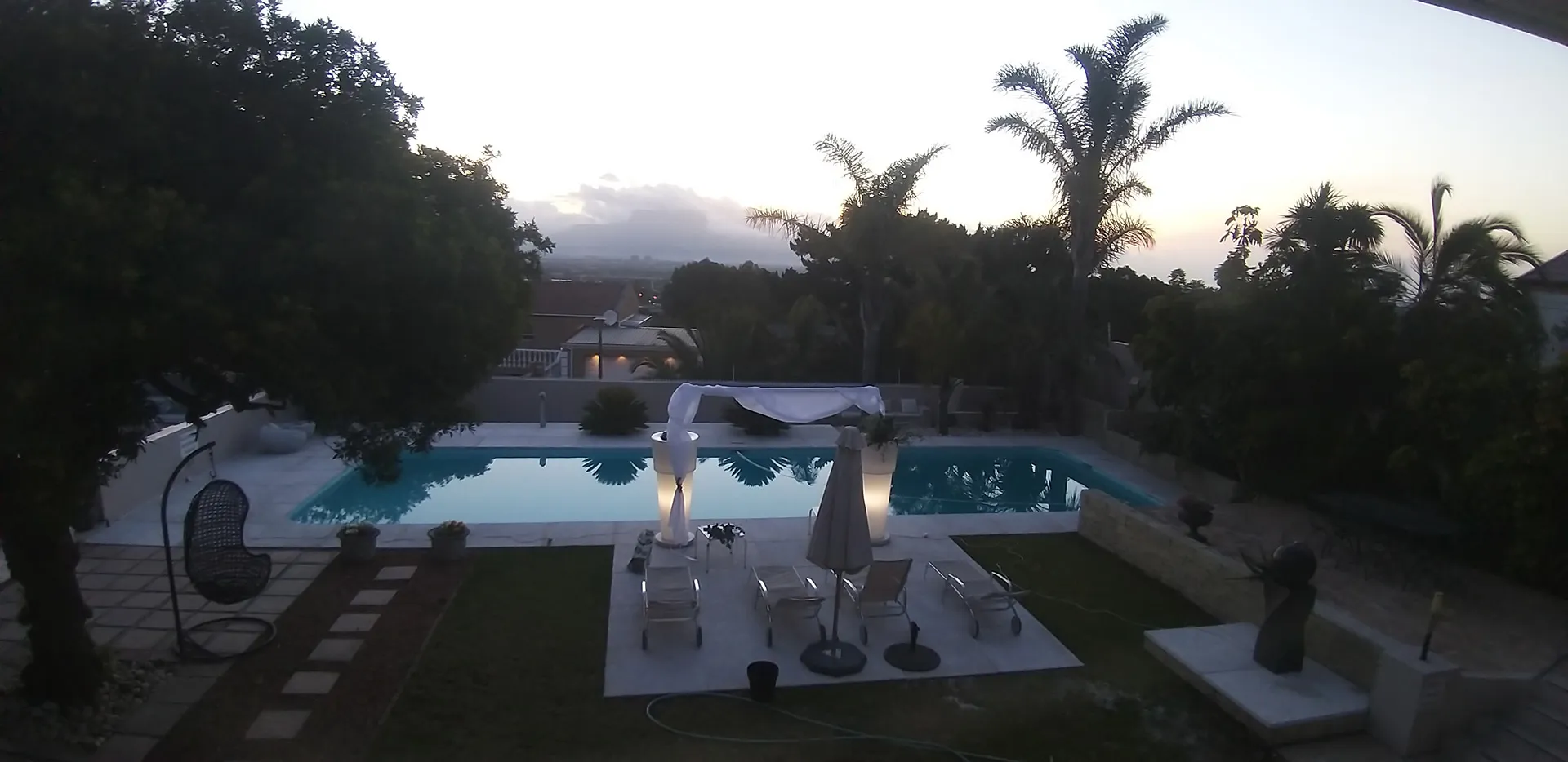 Swimming pool in a lush garden with lounge chairs and palm trees at sunset