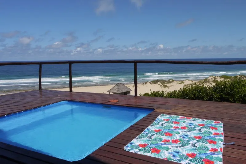 Small pool on wooden deck overlooking beach with colorful towel beside it
