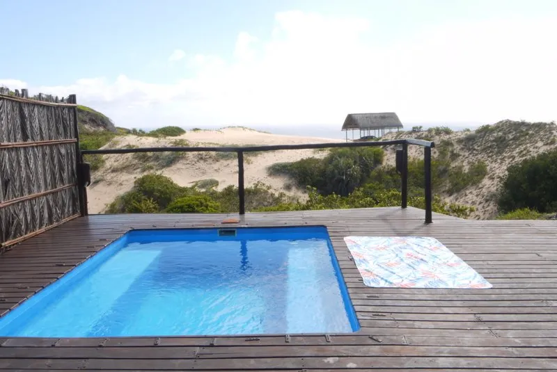 Small pool on wooden deck with ocean view and sand dunes in background