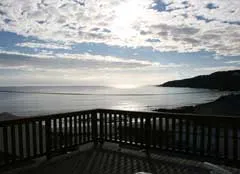 Wooden deck overlooking ocean with hills in the background under a cloudy sky