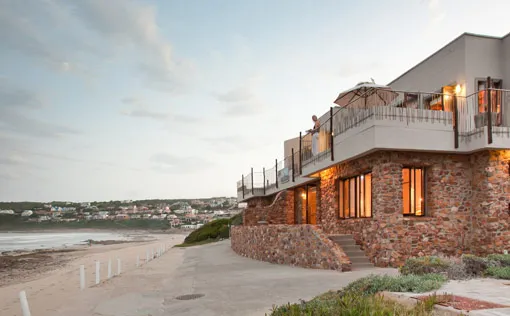 Beachfront house with stone exterior and balcony overlooking the ocean at sunset