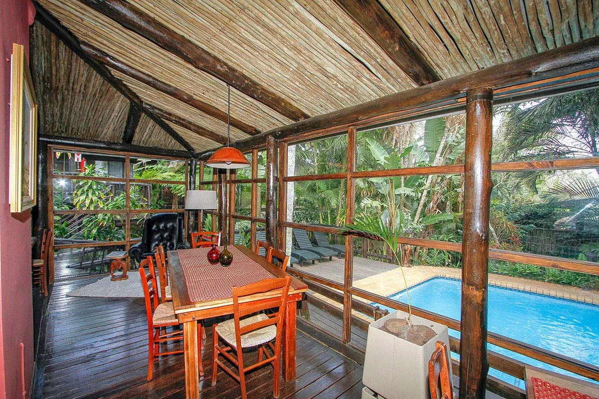 Wooden dining area with pool view surrounded by lush greenery