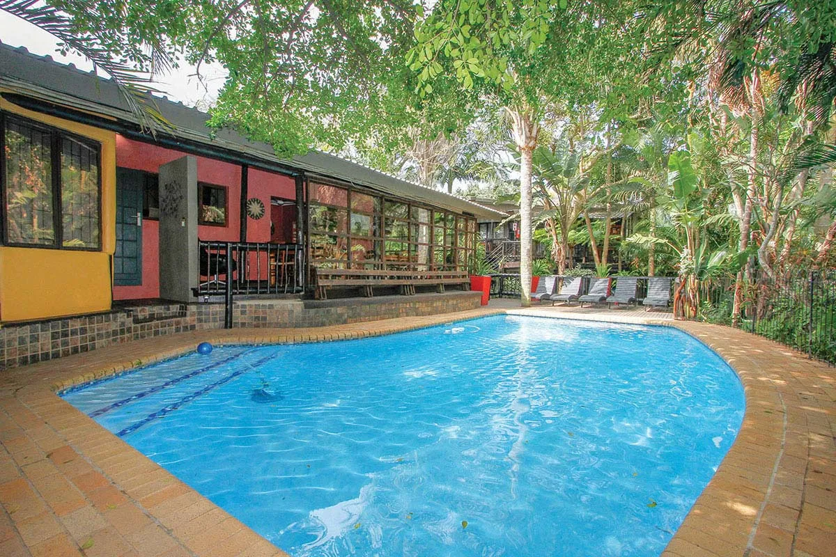 Swimming pool with colorful building and lounge chairs in a lush garden setting