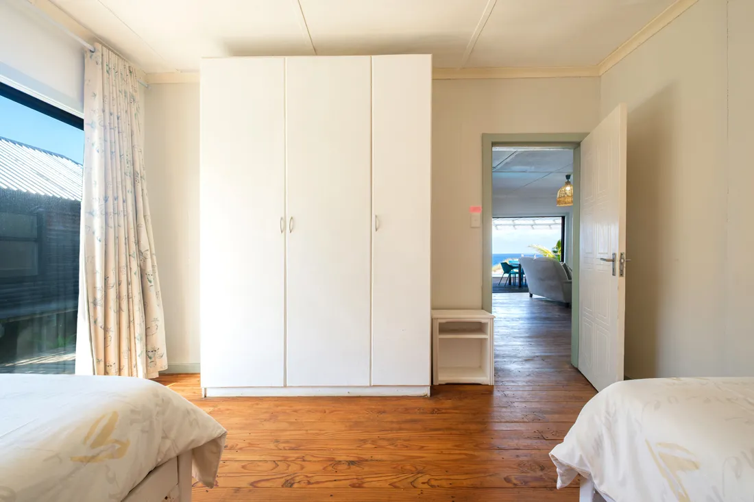 Bedroom with wooden floor white wardrobe two beds and open door to patio