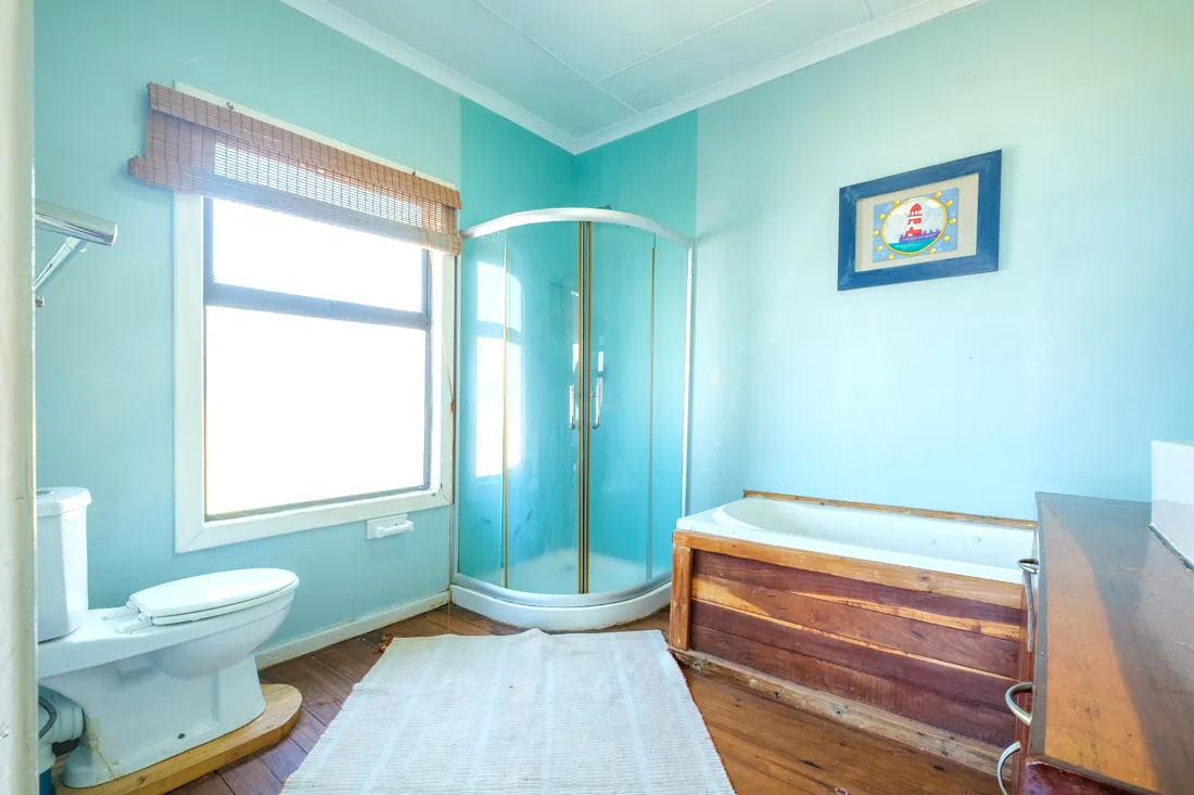 Light blue bathroom with wooden tub glass shower toilet and window
