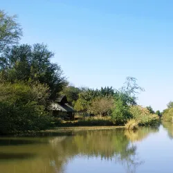 A small hut by a calm river with trees and clear blue sky