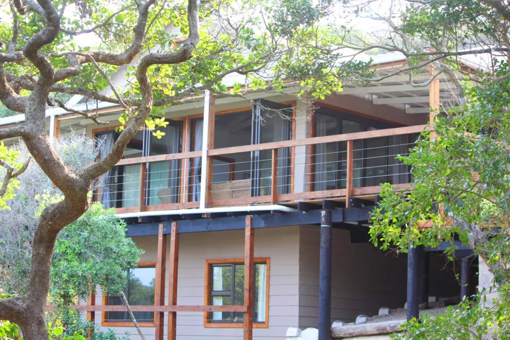 Wooden house with large windows and balcony surrounded by trees