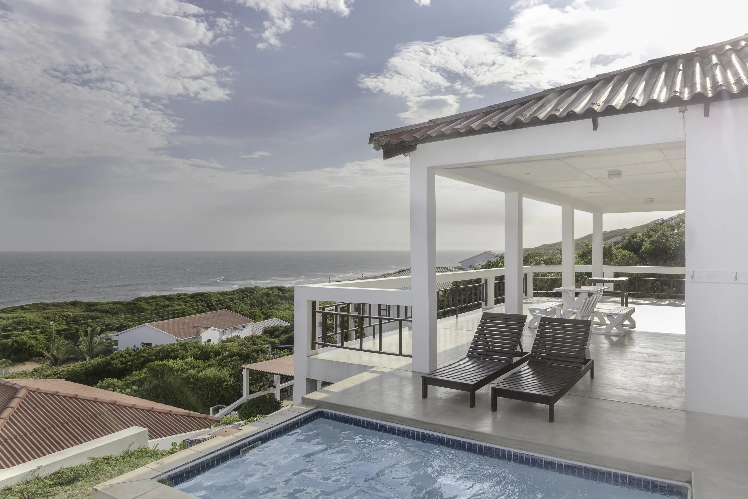 Modern house with pool lounge chairs and ocean view on a sunny day