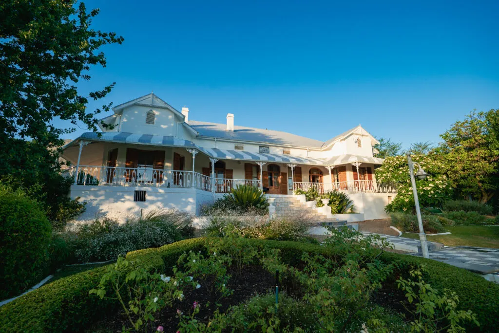 Large white house with a veranda surrounded by greenery and trees