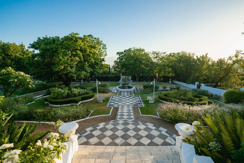 Garden with a central checkered pathway fountain and surrounding greenery under blue sky