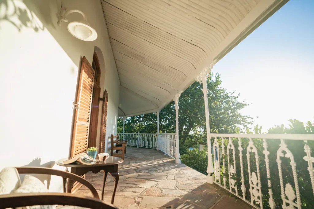 Wooden chairs on a covered porch with ornate railings overlooking a garden
