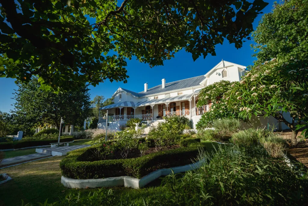 White house with a garden surrounded by trees and greenery under a blue sky