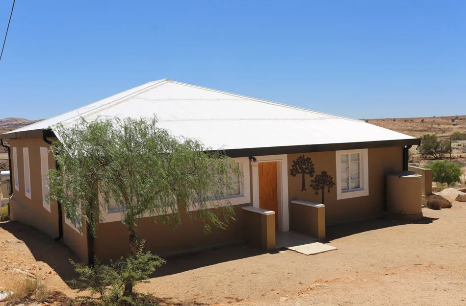 Singlestory house with white roof and tree in front desert landscape