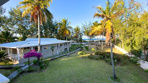 White house surrounded by palm trees and green lawn with ocean in background
