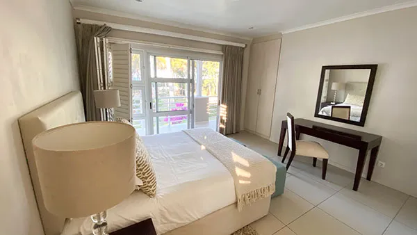 Modern bedroom with large bed desk mirror and sliding glass doors to balcony