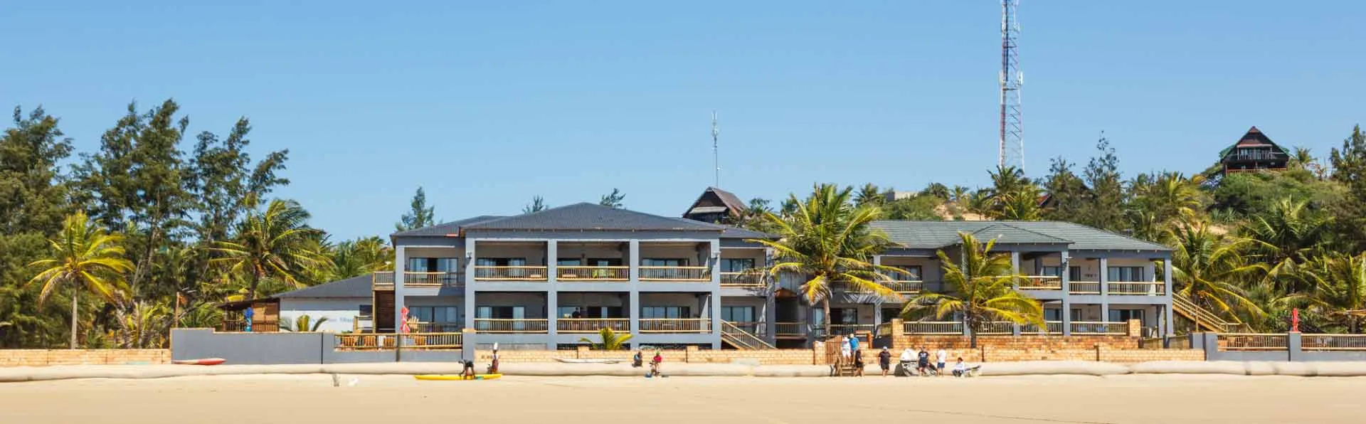 Beachfront resort with large building palm trees and people on the sand