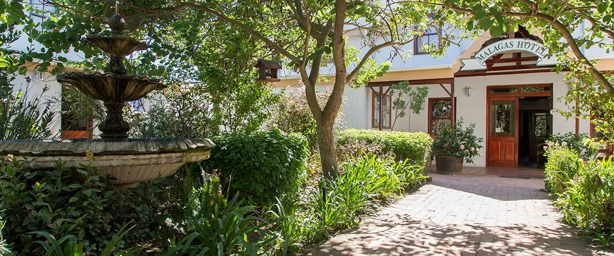 Pathway to a building entrance with a fountain and lush greenery