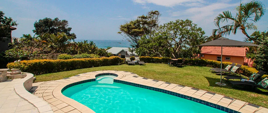 Swimming pool in a garden with ocean view and lounge chairs