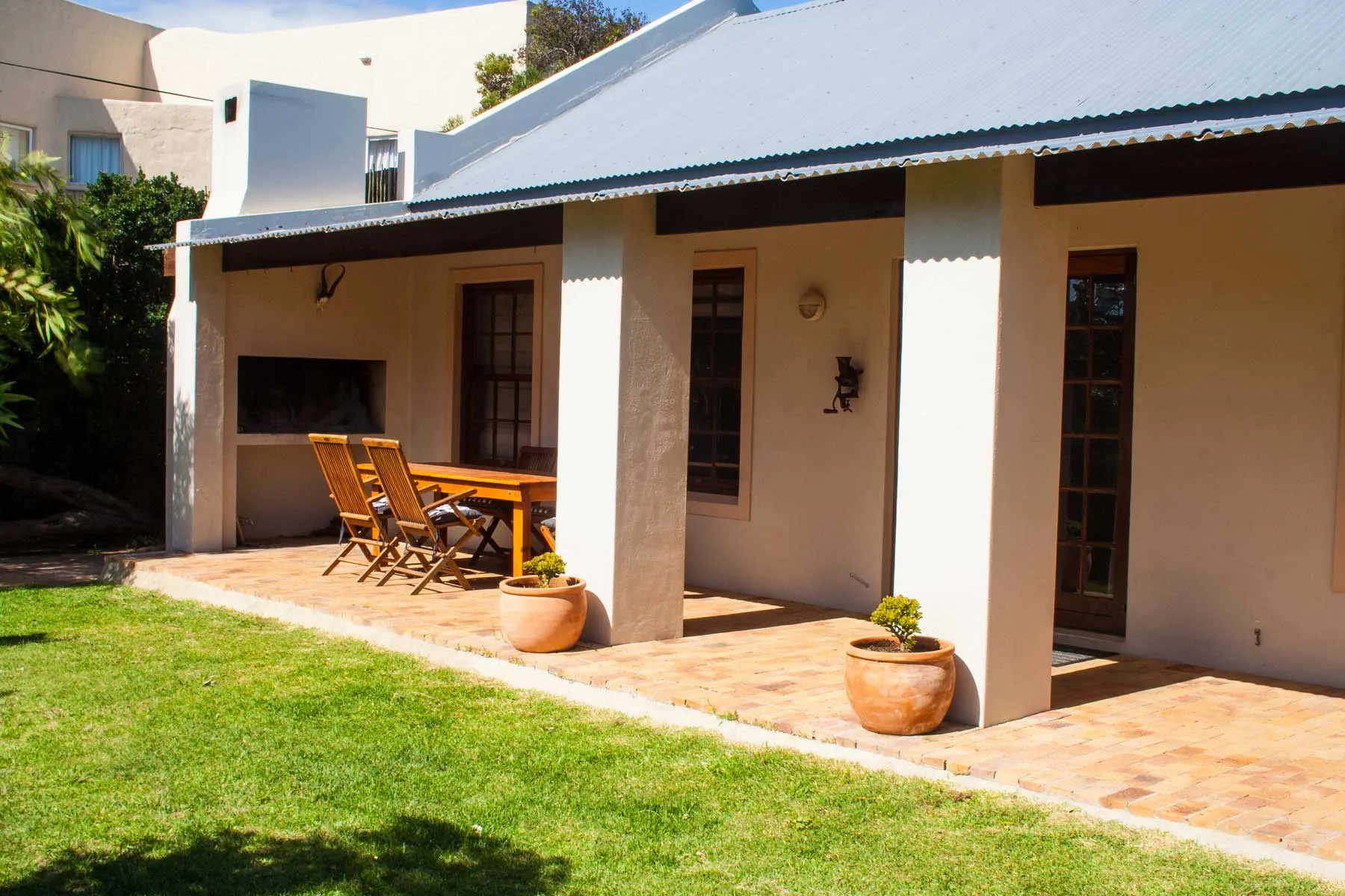 Patio with table chairs potted plants and a house with a corrugated roof