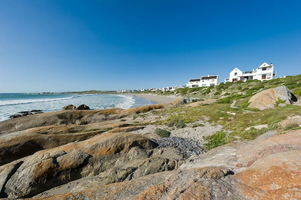 Rocky coastline with white houses on a grassy hill under a blue sky