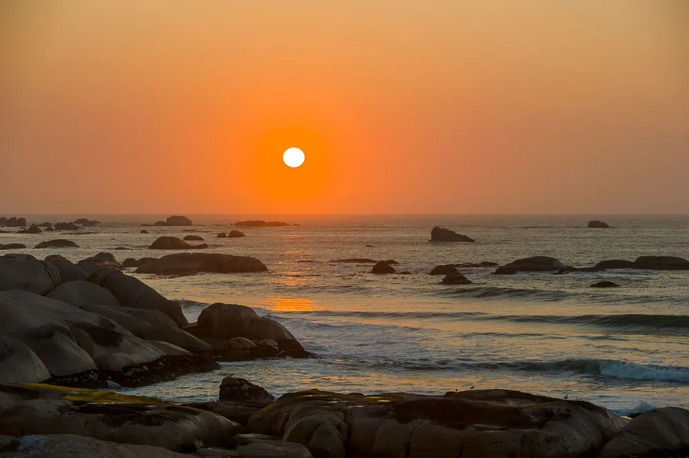 Sunset over ocean with rocky shoreline in the foreground